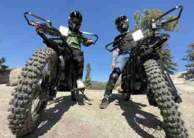 Lake Tahoe electric dirt bike tour: family duo in protective gear standing beside high-performance fat-tire e-bikes on rocky Sierra overlook, blue sky and pine forest backdrop – Tahoe Outdoor Adventures South Lake Tahoe