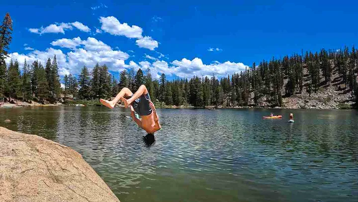Guest jumping off a granite cliff into a clear alpine lake
