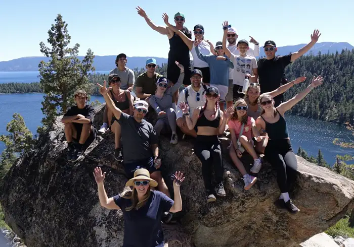 Large group of hikers cheering on a boulder above Emerald Bay