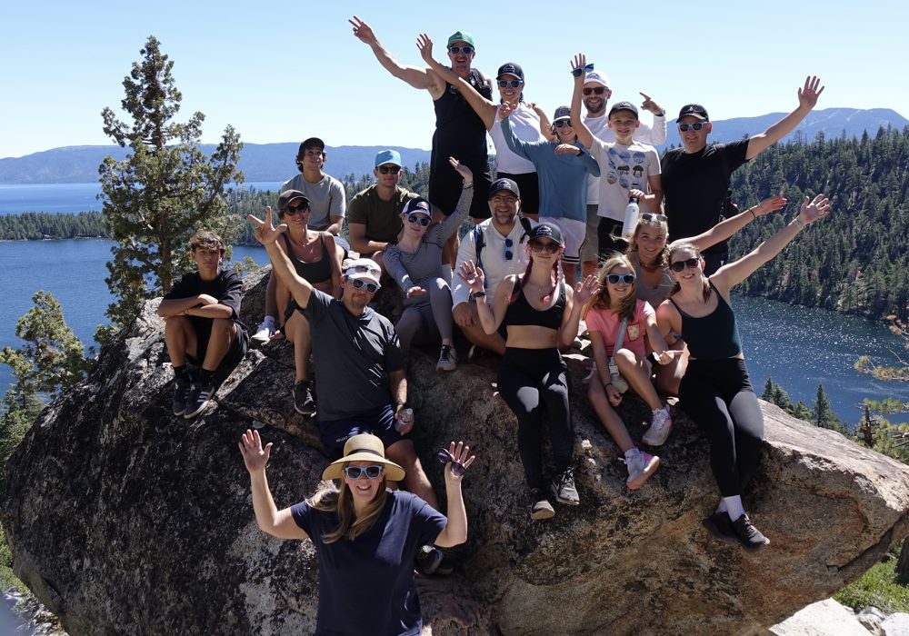 Large group of hikers cheering on a boulder above Emerald Bay