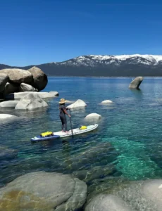 Paddle boarder on clear water among granite boulders on Lake Tahoe