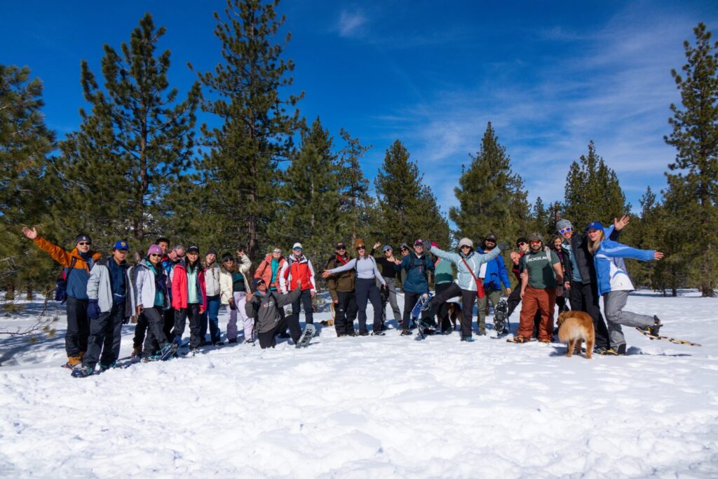 Big group waving on a snowshoe tour under tall pines near South Lake Tahoe