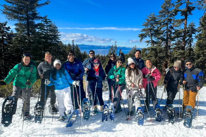 Group of guests on snowshoes with Lake Tahoe and snowy peaks behind them
