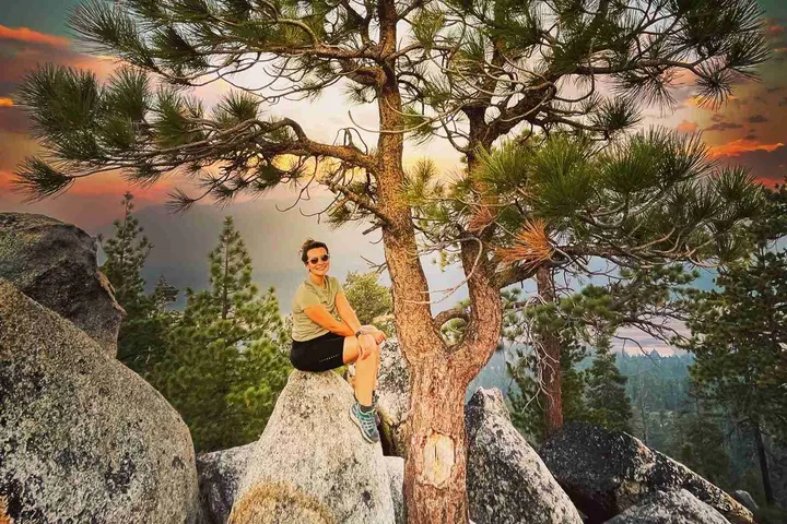 Hiker sitting on a granite boulder under a pine tree at sunset above Lake Tahoe
